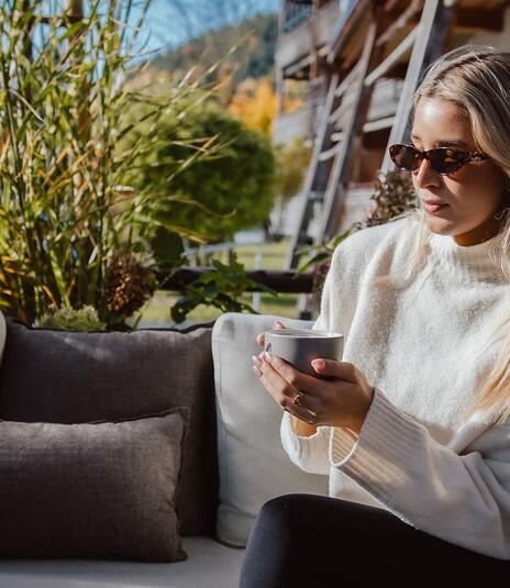 Lady drinking coffee in the sun on a garden sofa